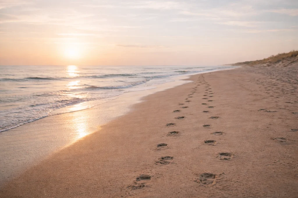 Plage au lever du soleil avec empreintes dans le sable, évoquant un chemin vers plus de sérénité et un nouvel élan de confiance en la vie